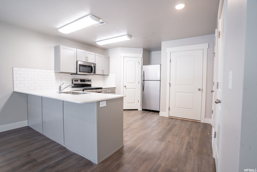 Kitchen featuring kitchen peninsula, stainless steel appliances, dark hardwood floors, and sink
