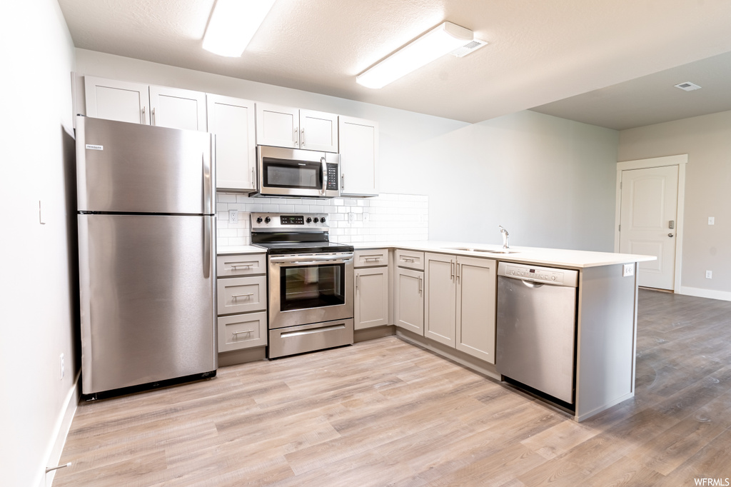 Kitchen featuring kitchen peninsula, light hardwood flooring, appliances with stainless steel finishes, backsplash, and sink