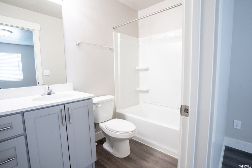 Full bathroom featuring vanity with extensive cabinet space, toilet, hardwood floors, and bathing tub / shower combination