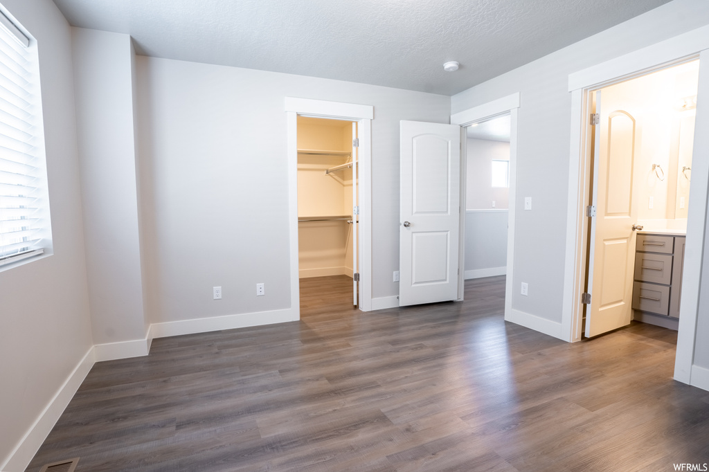 Unfurnished bedroom featuring multiple windows, ensuite bathroom, a spacious closet, dark hardwood floors, and a closet