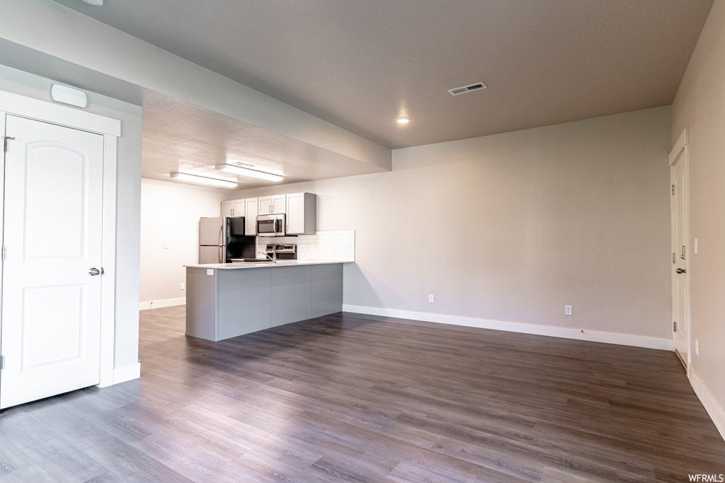 Kitchen with kitchen peninsula, dark hardwood flooring, backsplash, stainless steel appliances, and white cabinetry