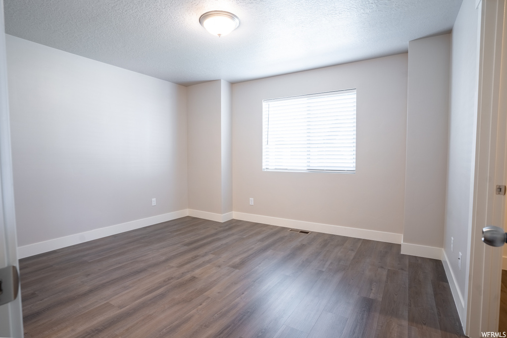Empty room with dark hardwood flooring and a textured ceiling