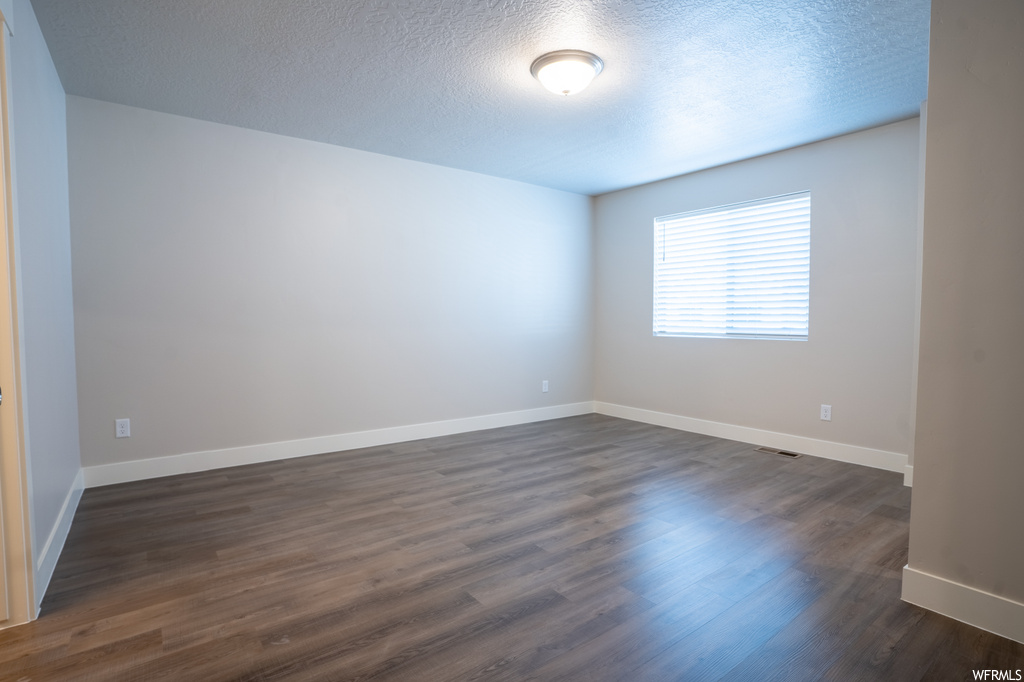 Spare room featuring dark hardwood floors and a textured ceiling