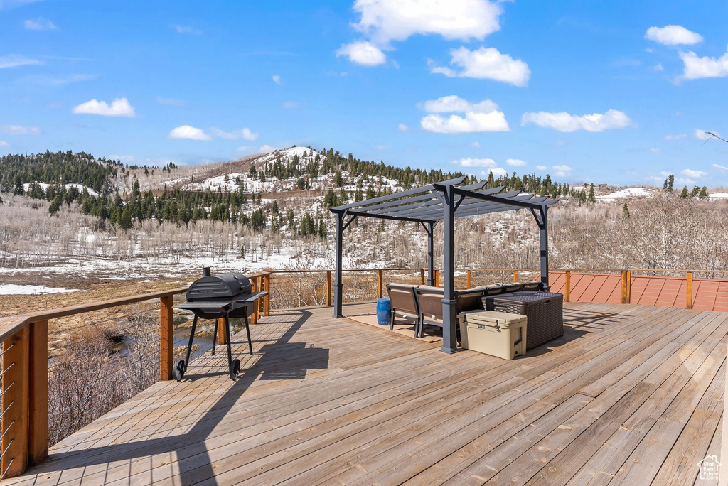 Snow covered deck with a mountain view, area for grilling, and a pergola