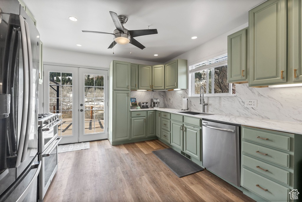 Kitchen featuring wood-type flooring, backsplash, stainless steel appliances, sink, and green cabinetry