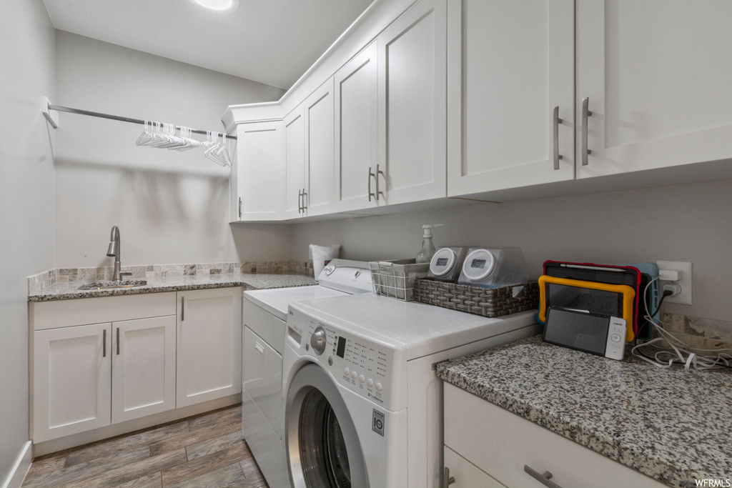 Laundry area featuring sink, washer and dryer, cabinets, and light hardwood flooring