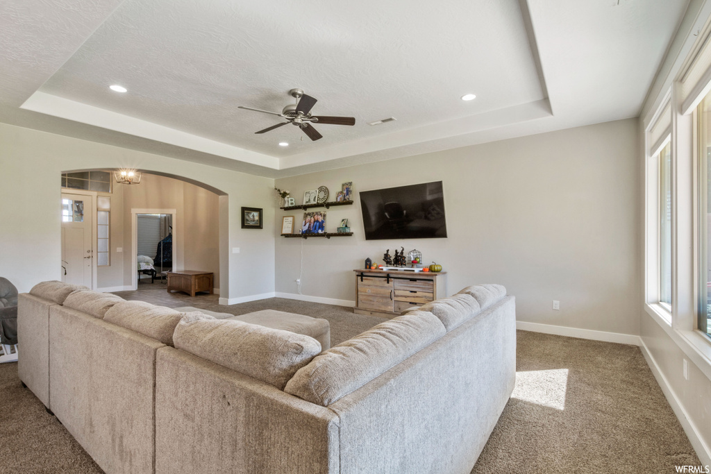 Living room featuring light carpet, ceiling fan, and a tray ceiling
