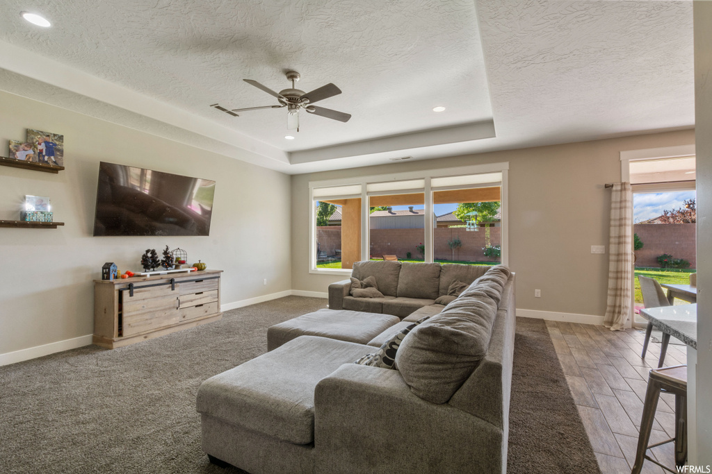 Hardwood floored living room with a textured ceiling, ceiling fan, and a tray ceiling