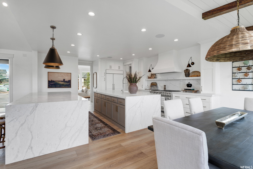 Kitchen featuring pendant lighting, a center island with sink, light hardwood flooring, white cabinets, and custom exhaust hood