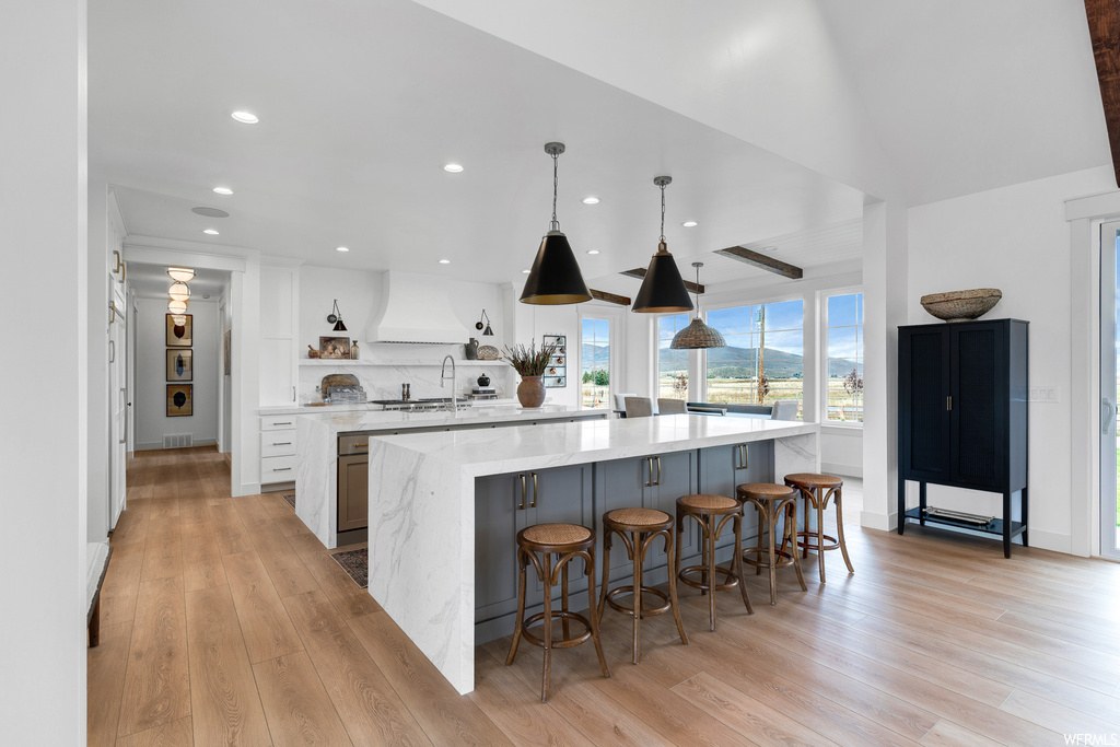 Kitchen featuring an island with sink, sink, light hardwood flooring, and pendant lighting