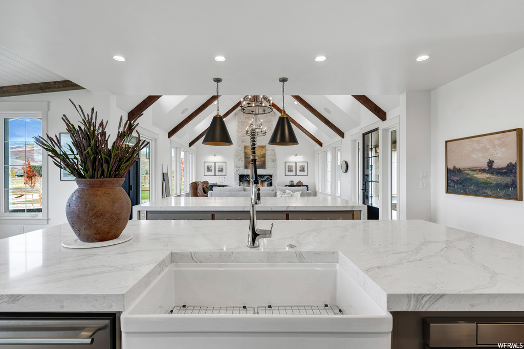 Kitchen featuring a center island with sink, light stone countertops, and vaulted ceiling with beams