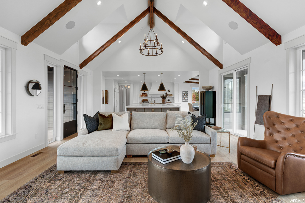Hardwood floored living room featuring vaulted ceiling high, an inviting chandelier, and beamed ceiling