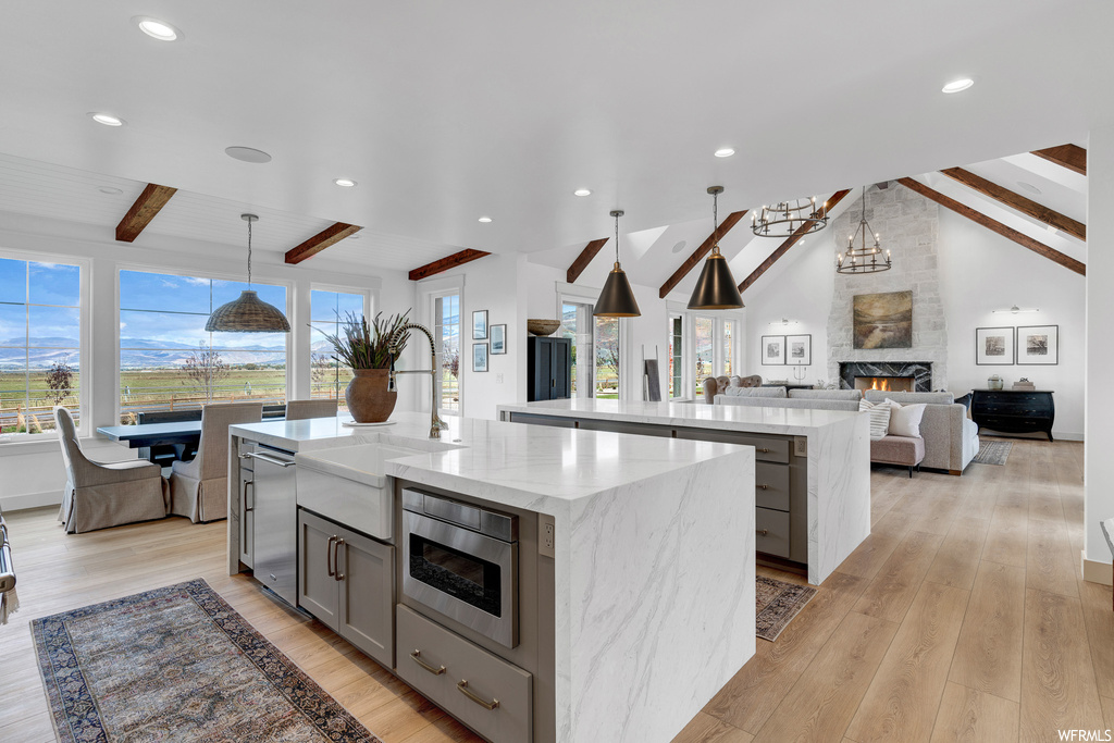 Kitchen featuring a fireplace, light hardwood floors, pendant lighting, a center island with sink, and beamed ceiling