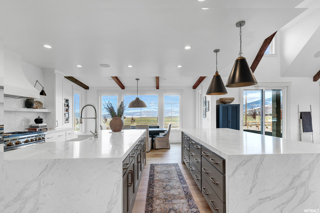 Kitchen featuring white cabinets, light stone counters, a kitchen island with sink, and plenty of natural light
