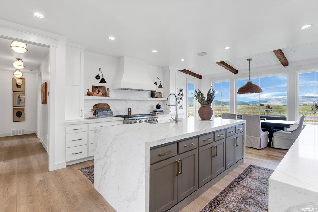 Kitchen featuring white cabinets, gray cabinetry, custom exhaust hood, light hardwood flooring, and beamed ceiling