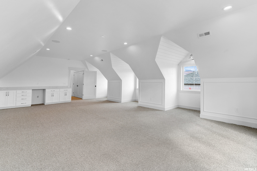 Additional living space with vaulted ceiling and light colored carpet