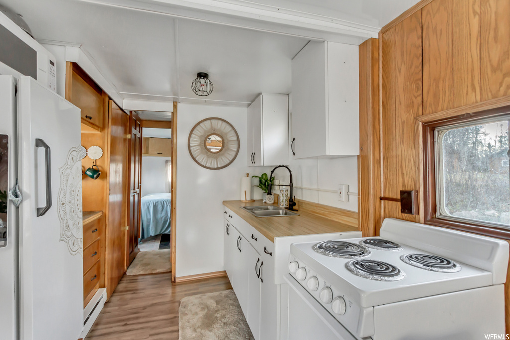 Kitchen with light hardwood / wood-style floors, sink, white fridge, range, and white cabinets