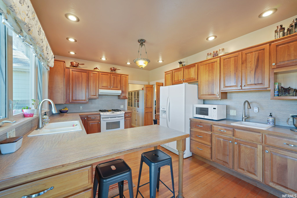 Kitchen with sink, backsplash, light hardwood floors, pendant lighting, and white appliances