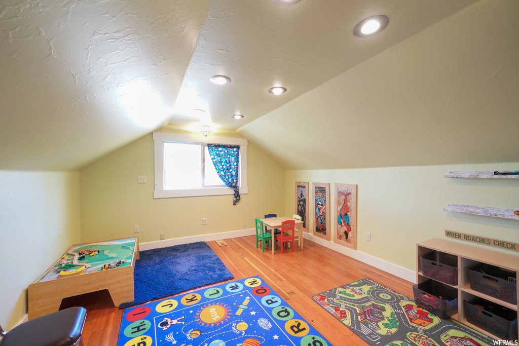 Game room with vaulted ceiling and light hardwood flooring