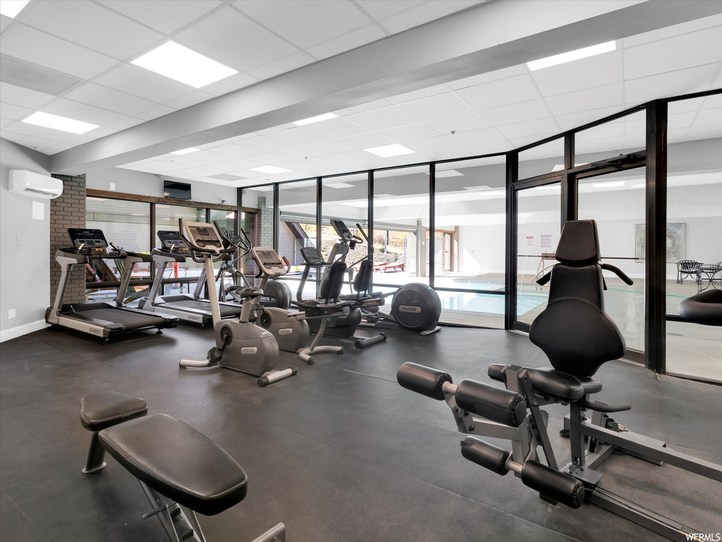 Workout area featuring expansive windows, an AC wall unit, and a paneled ceiling