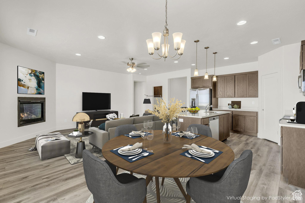 Dining room with ceiling fan with notable chandelier, light hardwood / wood-style floors, and sink