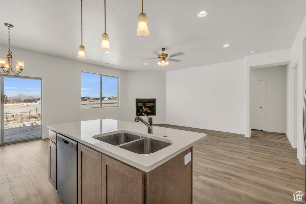 Kitchen with ceiling fan with notable chandelier, stainless steel dishwasher, light hardwood / wood-style floors, an island with sink, and sink