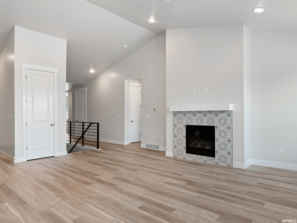 Unfurnished living room featuring a tiled fireplace, vaulted ceiling high, and light hardwood flooring