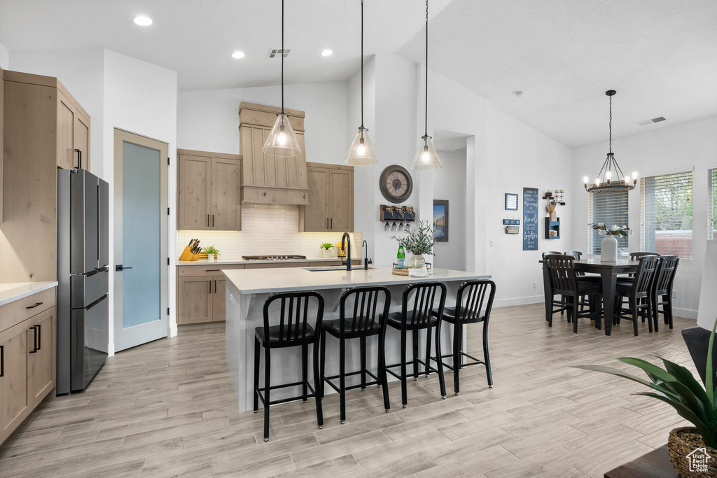 Kitchen featuring a center island with sink, stainless steel fridge, tasteful backsplash, and pendant lighting