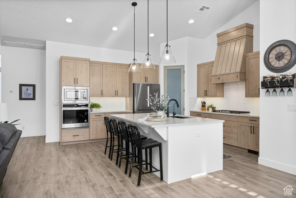 Kitchen featuring light wood-type flooring, appliances with stainless steel finishes, sink, tasteful backsplash, and an island with sink