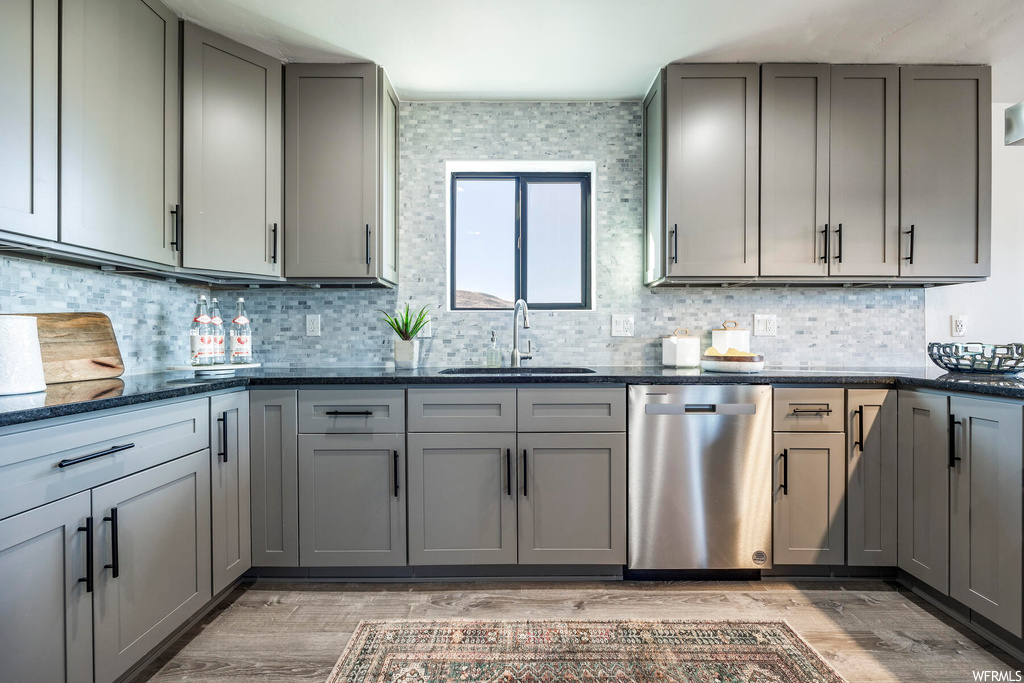 Kitchen featuring sink, light hardwood / wood-style flooring, dark stone counters, dishwasher, and backsplash