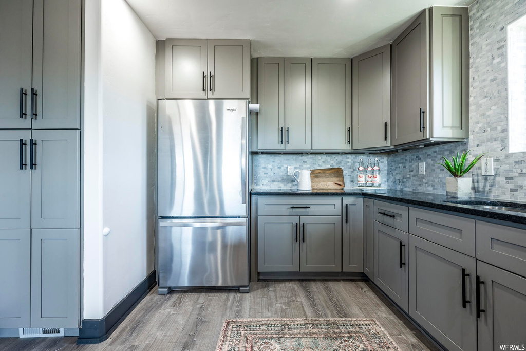 Kitchen featuring dark stone countertops, stainless steel fridge, gray cabinets, backsplash, and light wood-type flooring