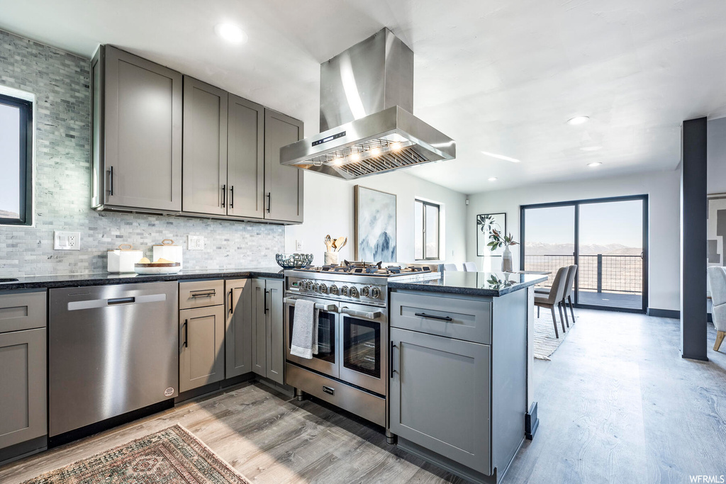 Kitchen with island exhaust hood, gray cabinetry, light hardwood / wood-style floors, stainless steel appliances, and kitchen peninsula