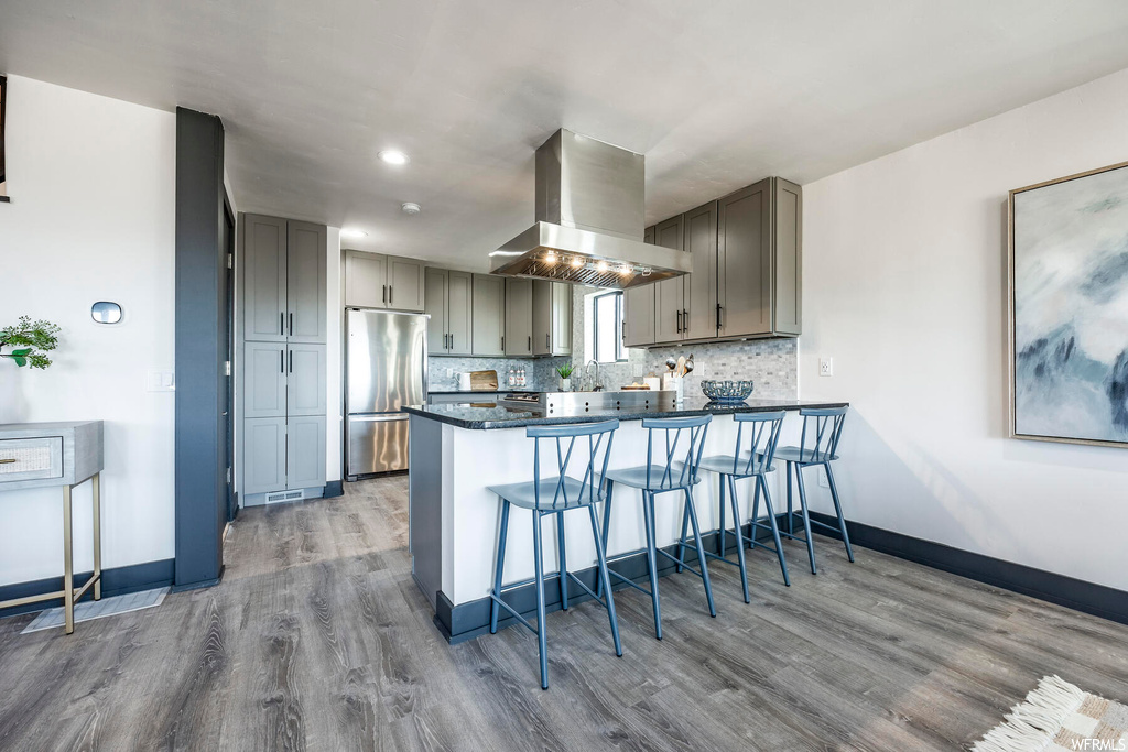 Kitchen featuring stainless steel refrigerator, island range hood, light hardwood / wood-style floors, and gray cabinets