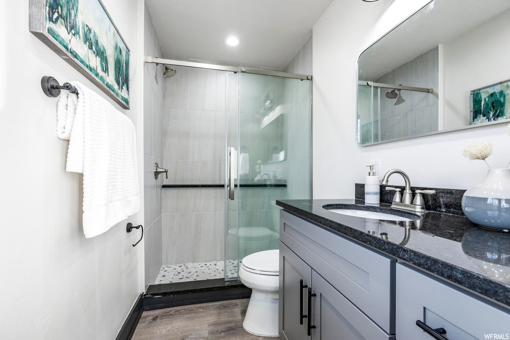 Bathroom featuring toilet, a shower with shower door, vanity with extensive cabinet space, and hardwood / wood-style flooring