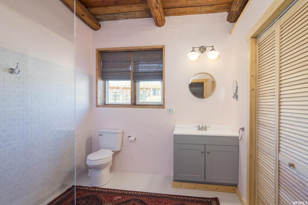 Bathroom with toilet, large vanity, beam ceiling, and tile flooring