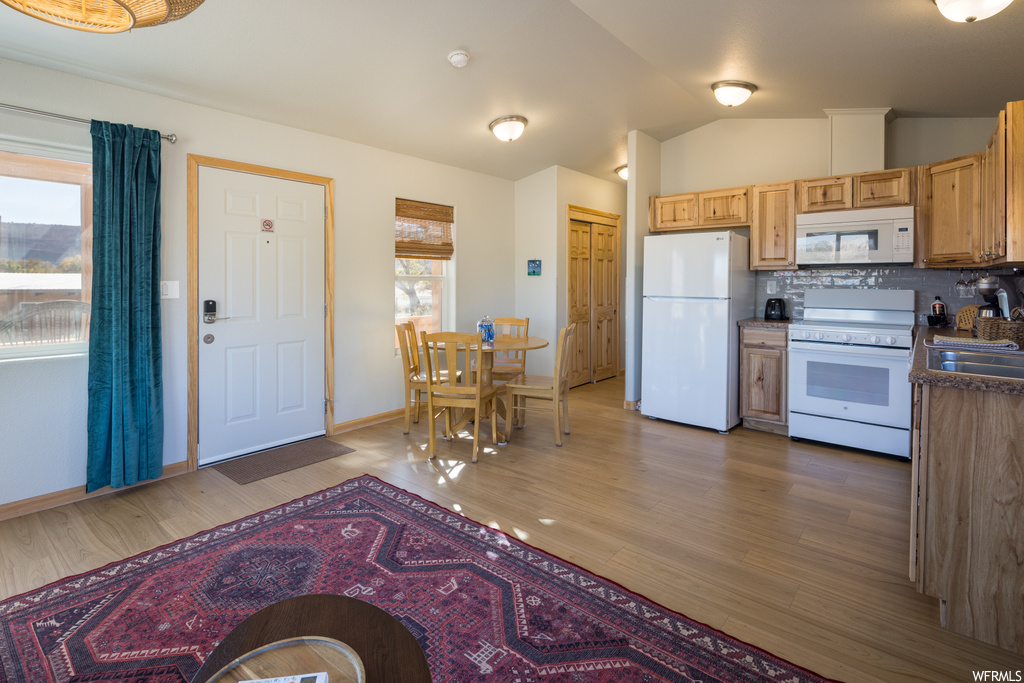 Kitchen featuring sink, white appliances, hardwood / wood-style flooring, lofted ceiling, and tasteful backsplash