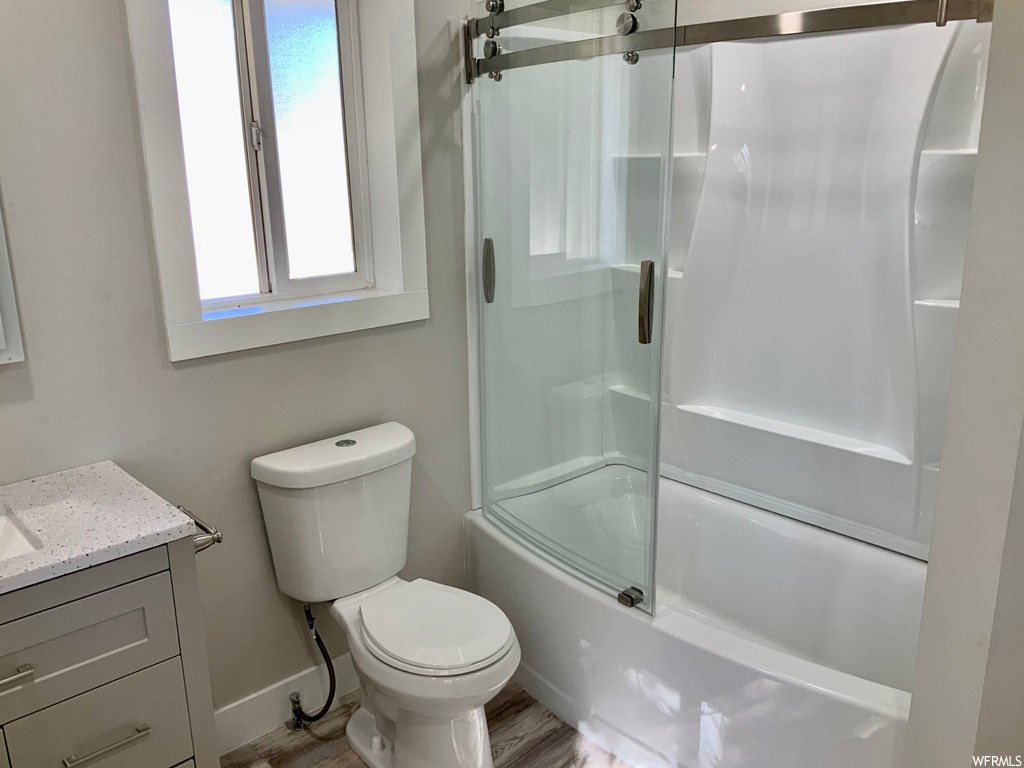 Full bathroom with bath / shower combo with glass door, wood-type flooring, toilet, and vanity