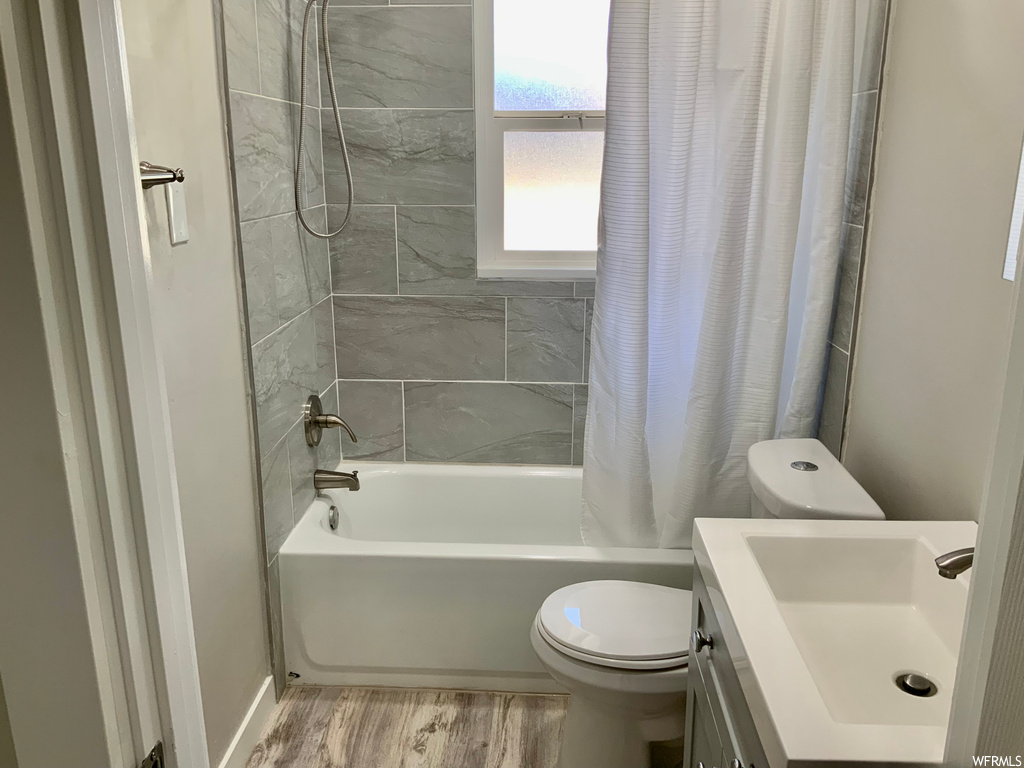 Full bathroom featuring toilet, vanity, hardwood floors, and shower / bathtub combination with curtain