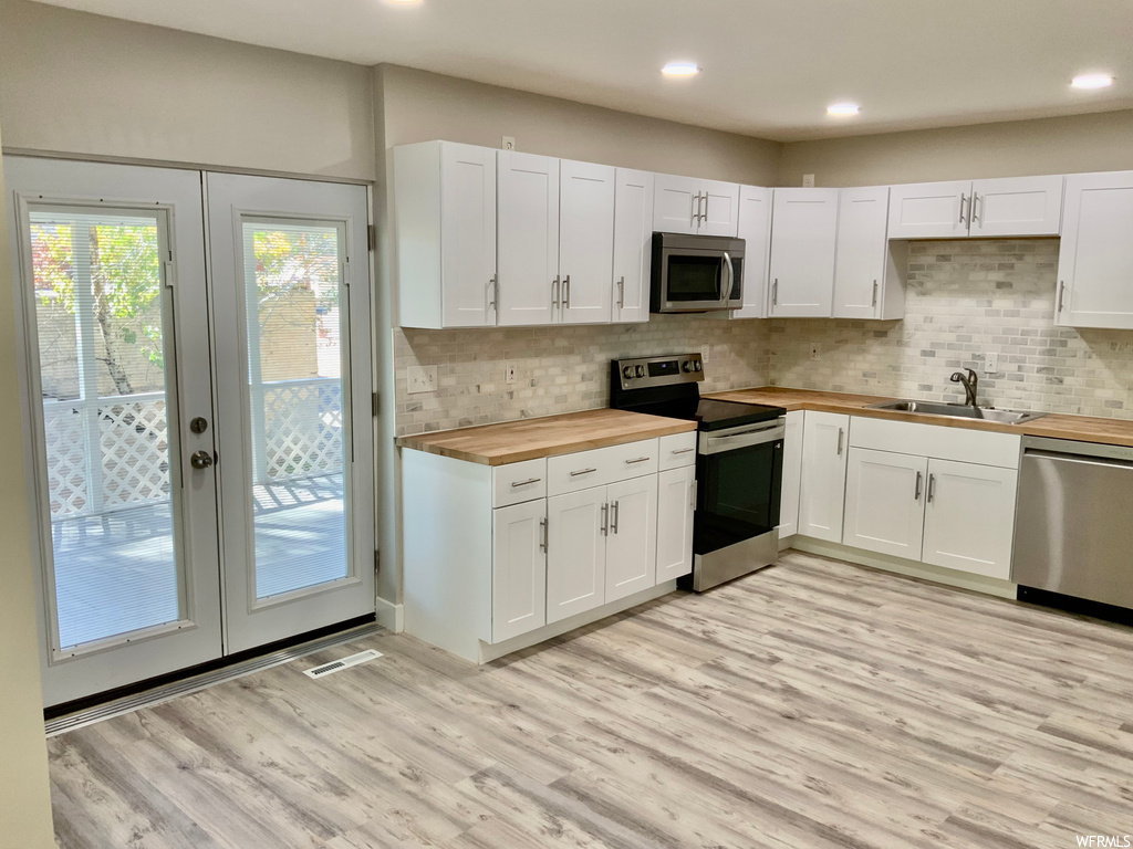 Kitchen featuring white cabinetry, stainless steel appliances, butcher block countertops, and light hardwood flooring