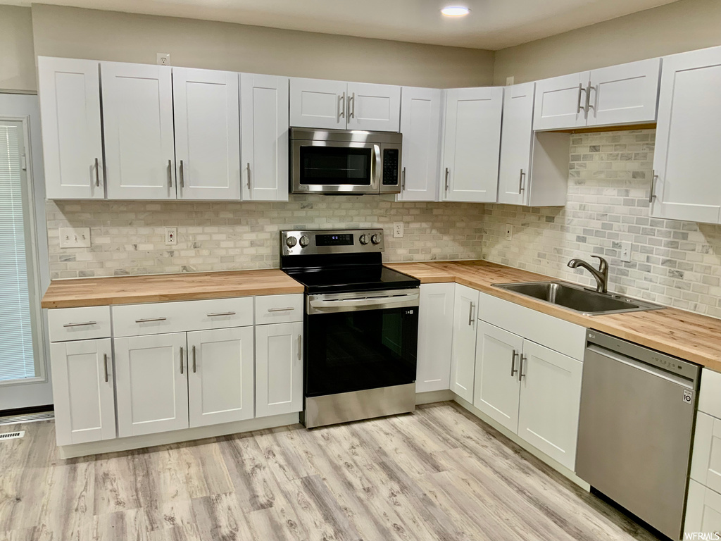Kitchen featuring white cabinets, butcher block counters, light hardwood floors, tasteful backsplash, and appliances with stainless steel finishes