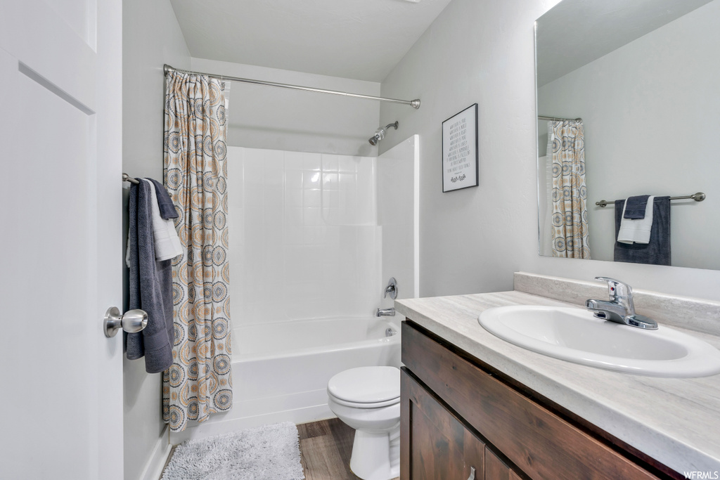 Full bathroom featuring hardwood flooring, shower / tub combo, vanity, and toilet