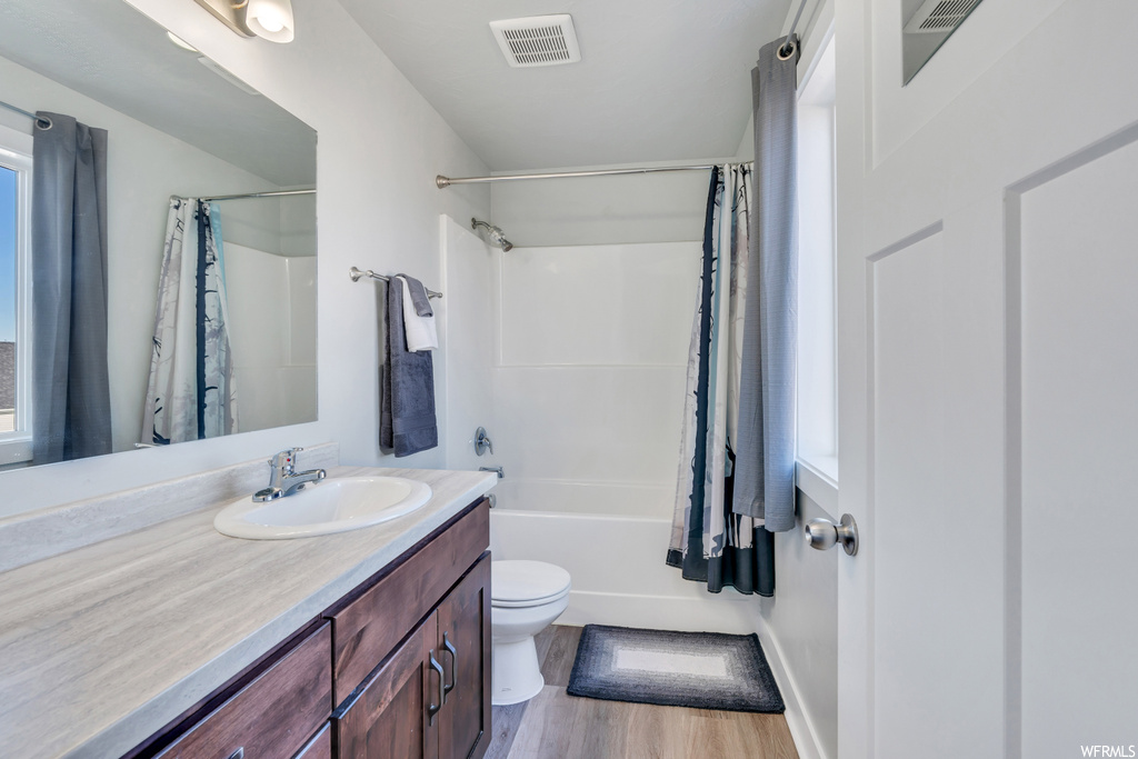 Full bathroom featuring vanity with extensive cabinet space, toilet, hardwood flooring, and shower / bath combination with curtain