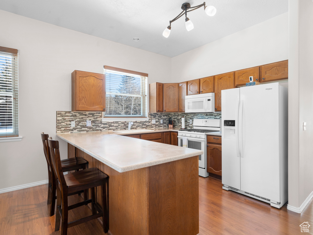 Kitchen with hardwood / wood-style floors, white appliances, a kitchen bar, kitchen peninsula, and backsplash