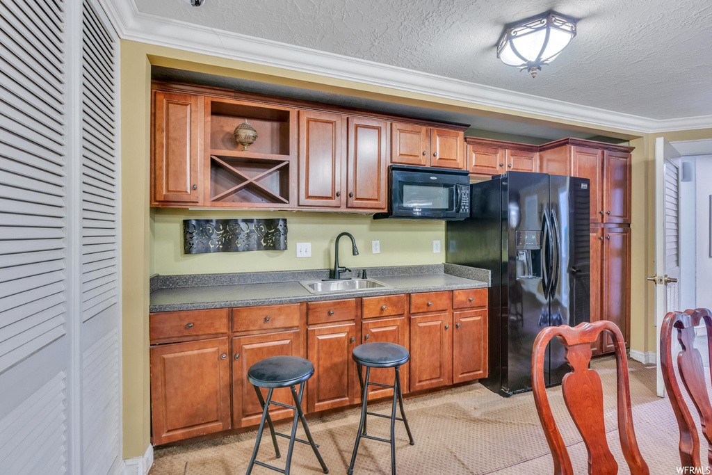 Kitchen featuring sink, light colored carpet, black appliances, a textured ceiling, and crown molding
