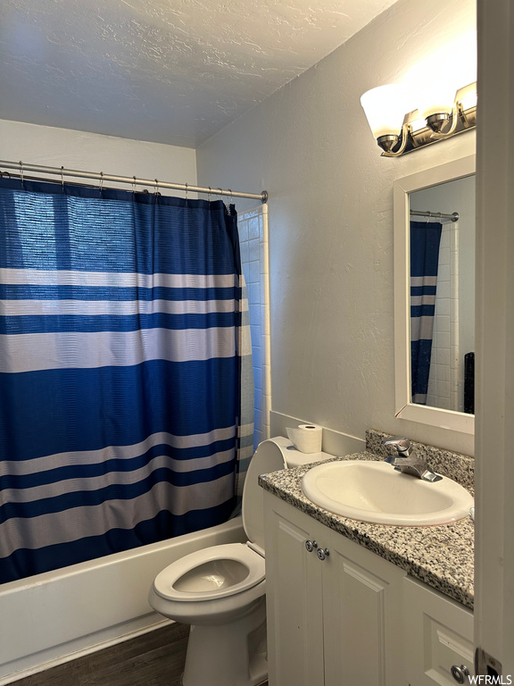 Full bathroom with hardwood flooring, toilet, shower / tub combo with curtain, and vanity
