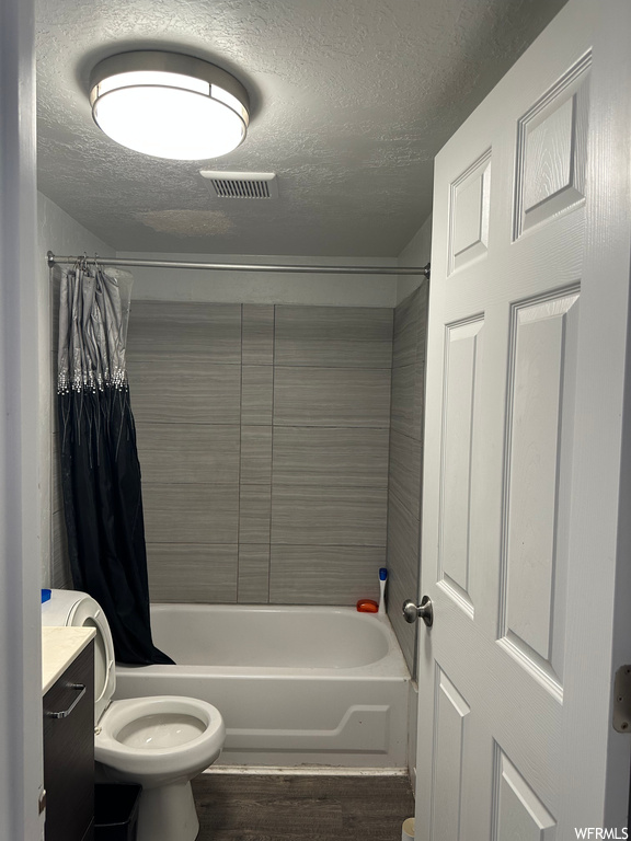 Full bathroom featuring toilet, vanity, a textured ceiling, shower / tub combo, and hardwood floors