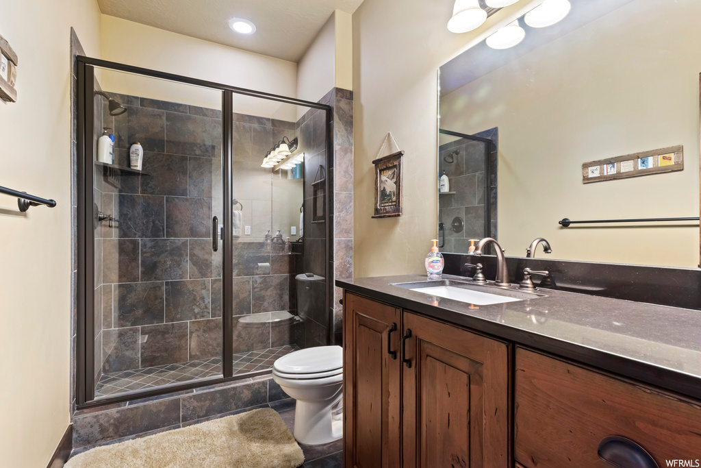 Bathroom featuring tile floors, toilet, a shower with door, and vanity