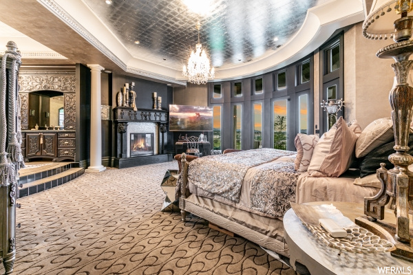 Bedroom with a fireplace, decorative columns, crown molding, an inviting chandelier, and a tray ceiling