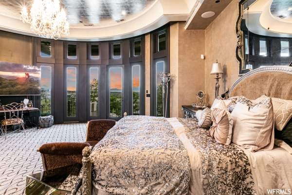 Bedroom featuring light colored carpet, a high ceiling, access to outside, a notable chandelier, and a tray ceiling