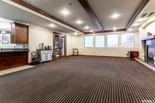 Interior space featuring bar area, beamed ceiling, dark colored carpet, and a fireplace